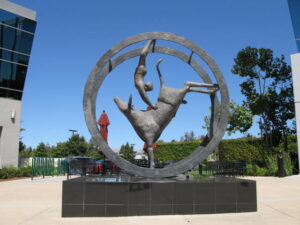 A sculpture of a human figure and a bull within a metal circle on a black base, set outdoors.
