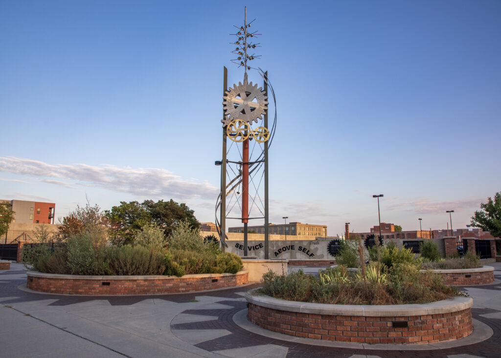 Tall sculpture with large gears surrounded by landscaped garden