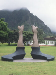Abstract sculptures on a green lawn with misty mountains and a building in the background.